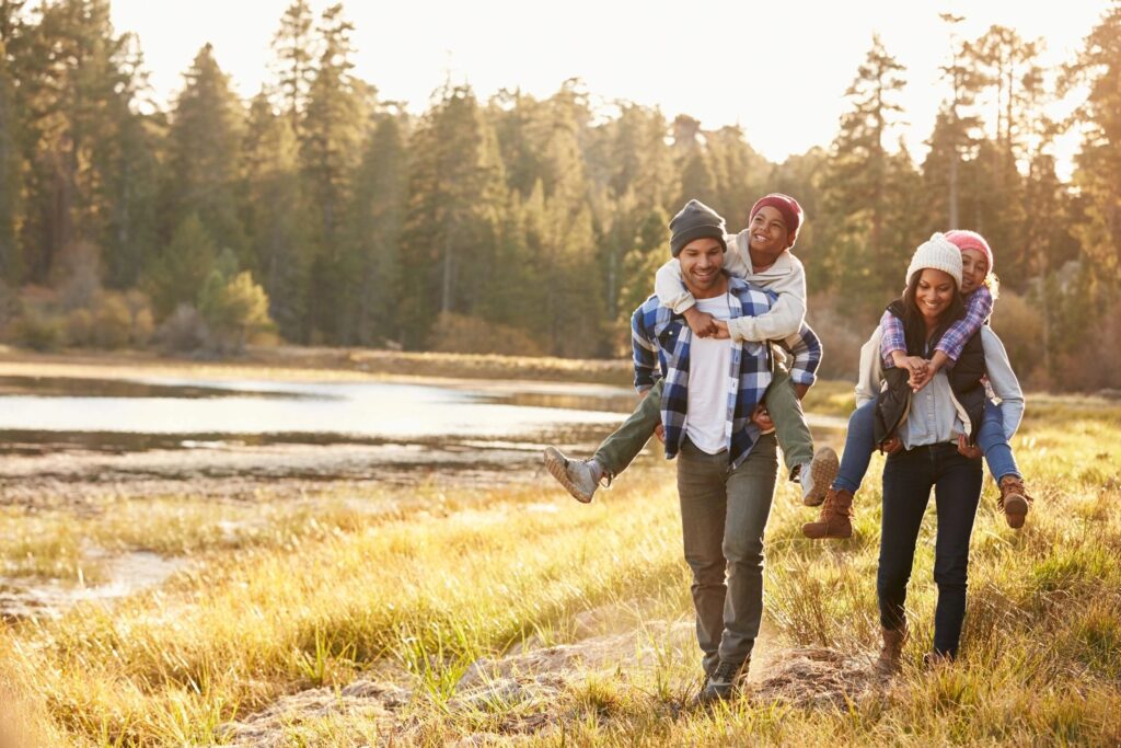 A family walks around a pond, surrounded by pine trees.